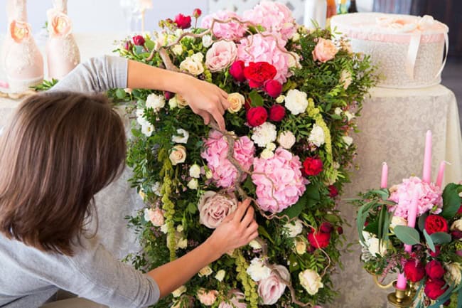 Florist at work. Woman making spring floral decorations the wedding table the bride and groom. Flowers candles a bottle of champagne. The vintage.
