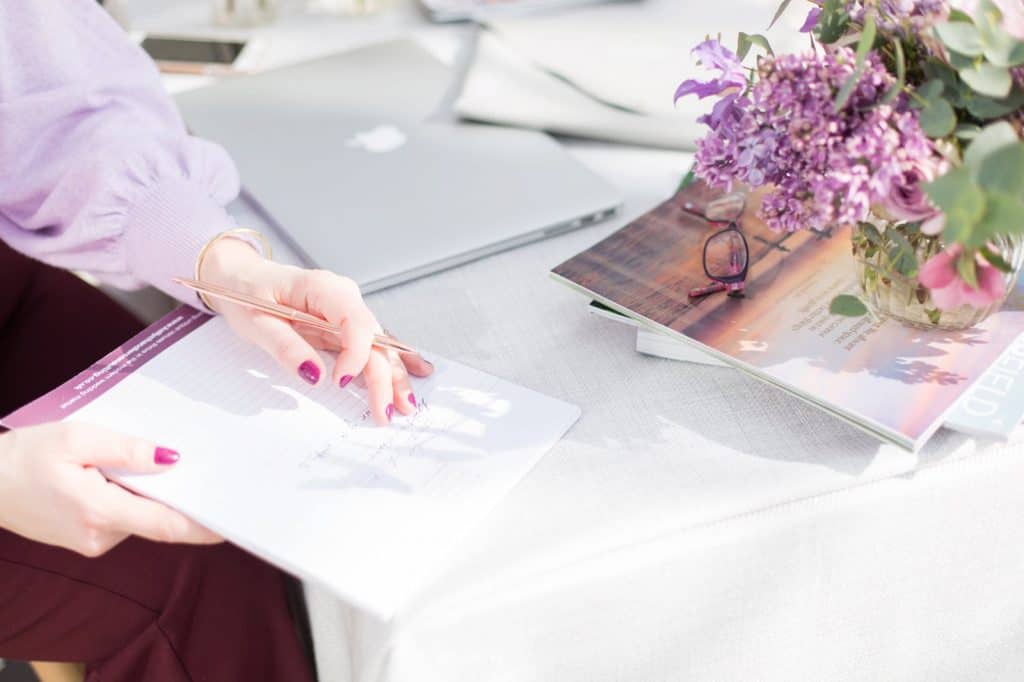 Close up of womans hands with purple nails writing on an A4 piece of paper