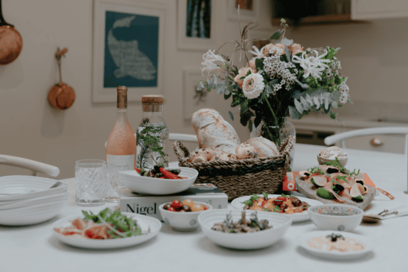 Elegant table setting with bread, salads, and floral centrepiece in a cosy kitchen.