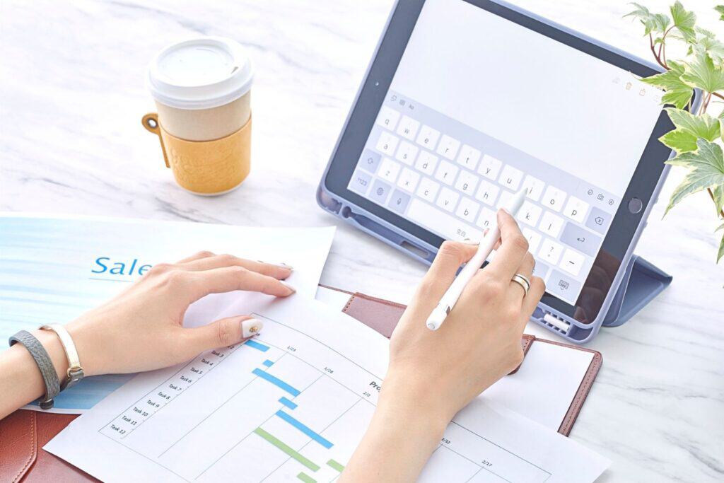 Woman working on sales data with tablet and charts in a bright workspace.