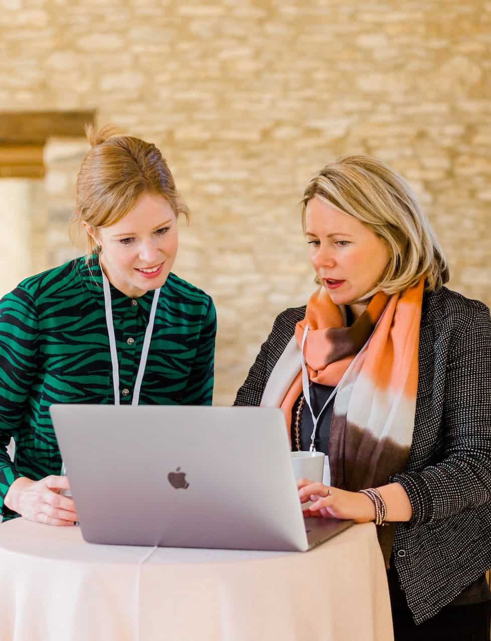Two women working together on a laptop at a professional event in the UK.