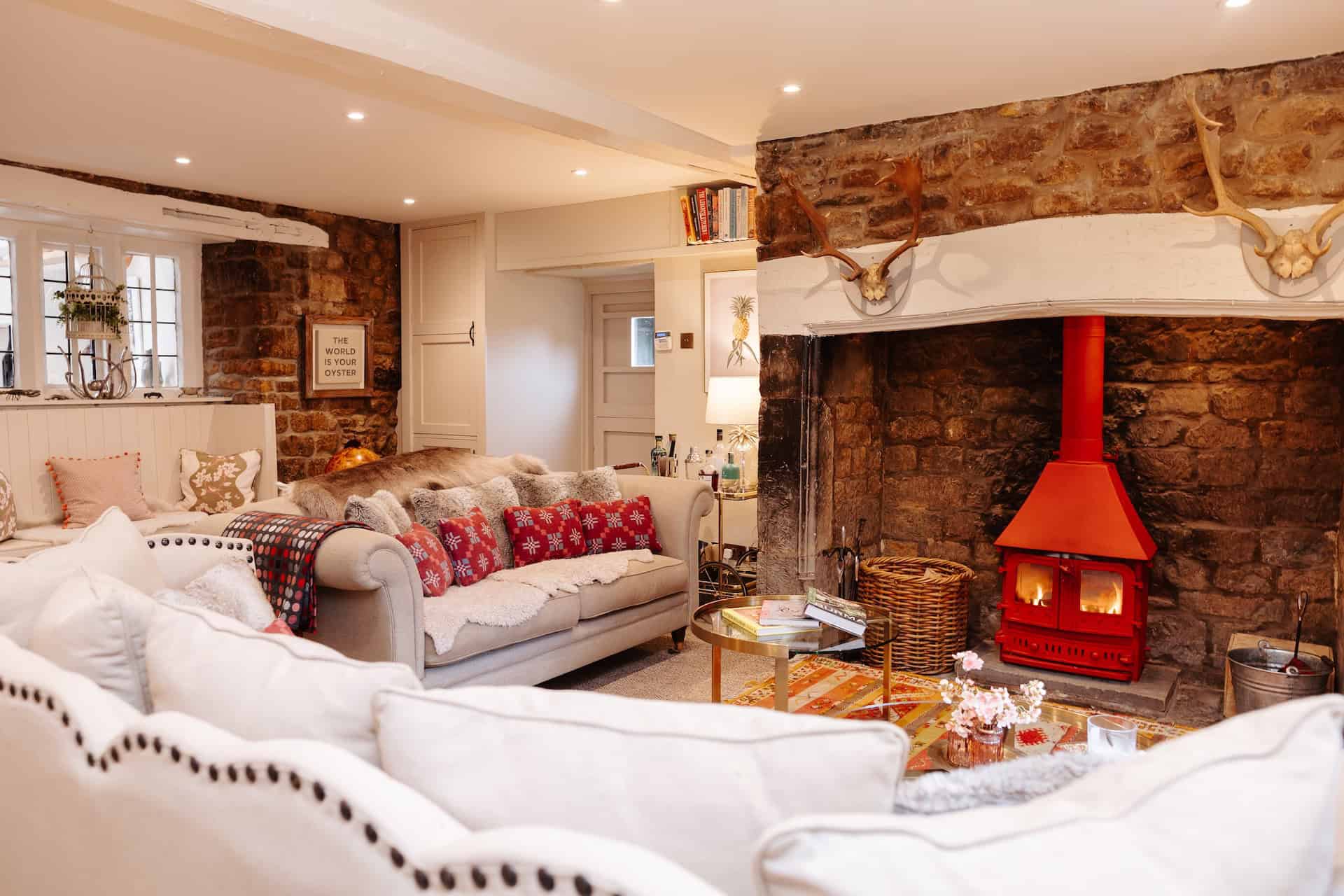 Cozy living room with exposed brick wall and red fireplace, decorated with cushions and books.