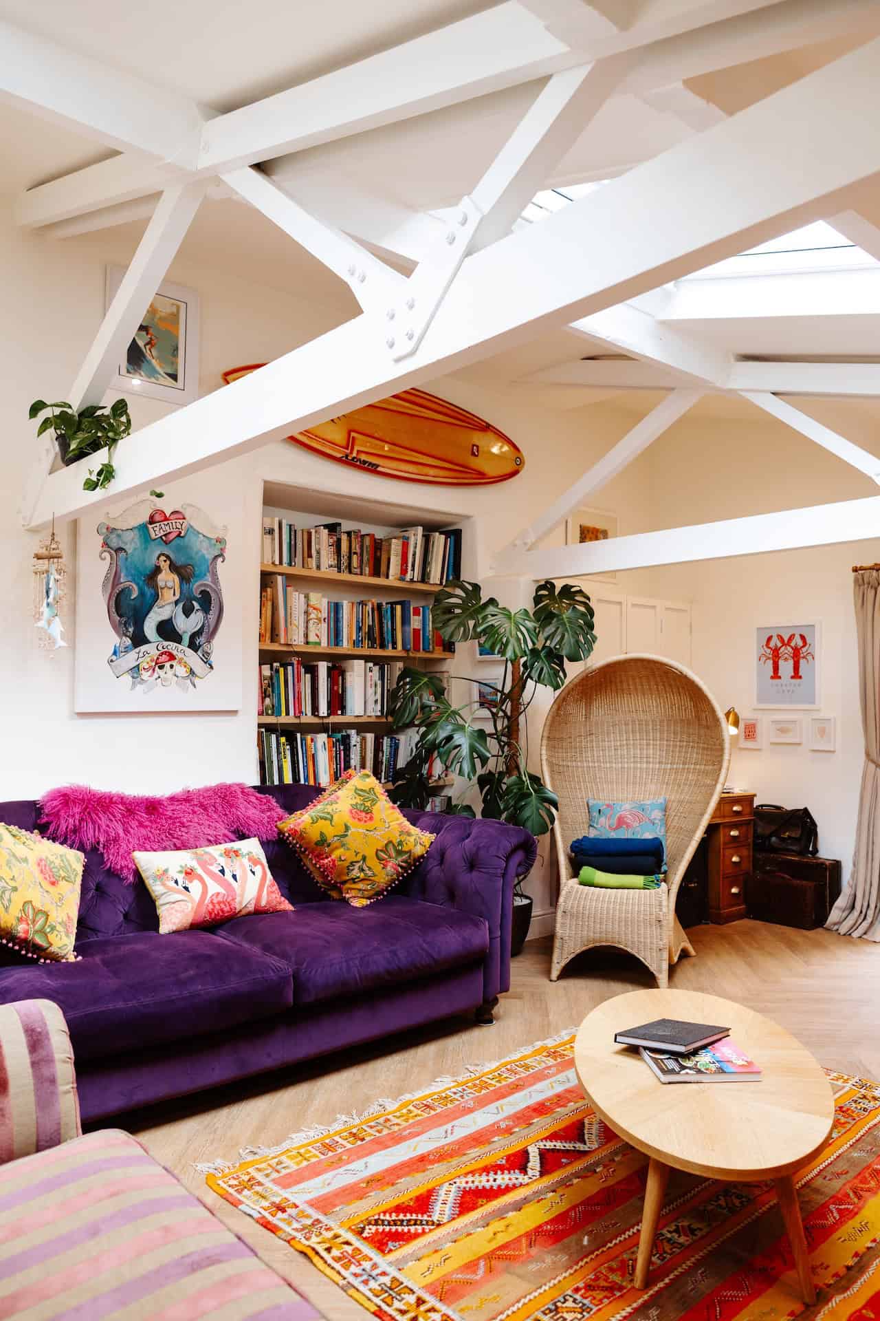 Cozy living room with colourful furniture and artwork, under white ceiling beams.