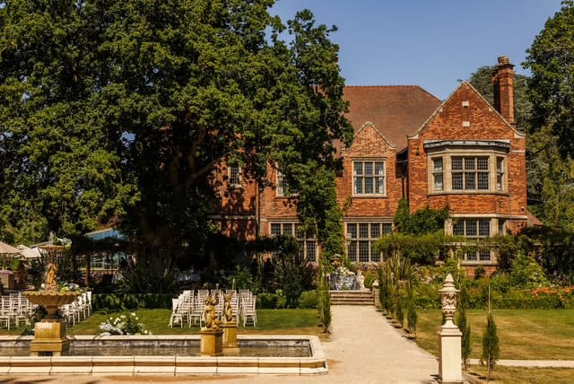 Elegant historic brick house with lush garden and fountain in front.
