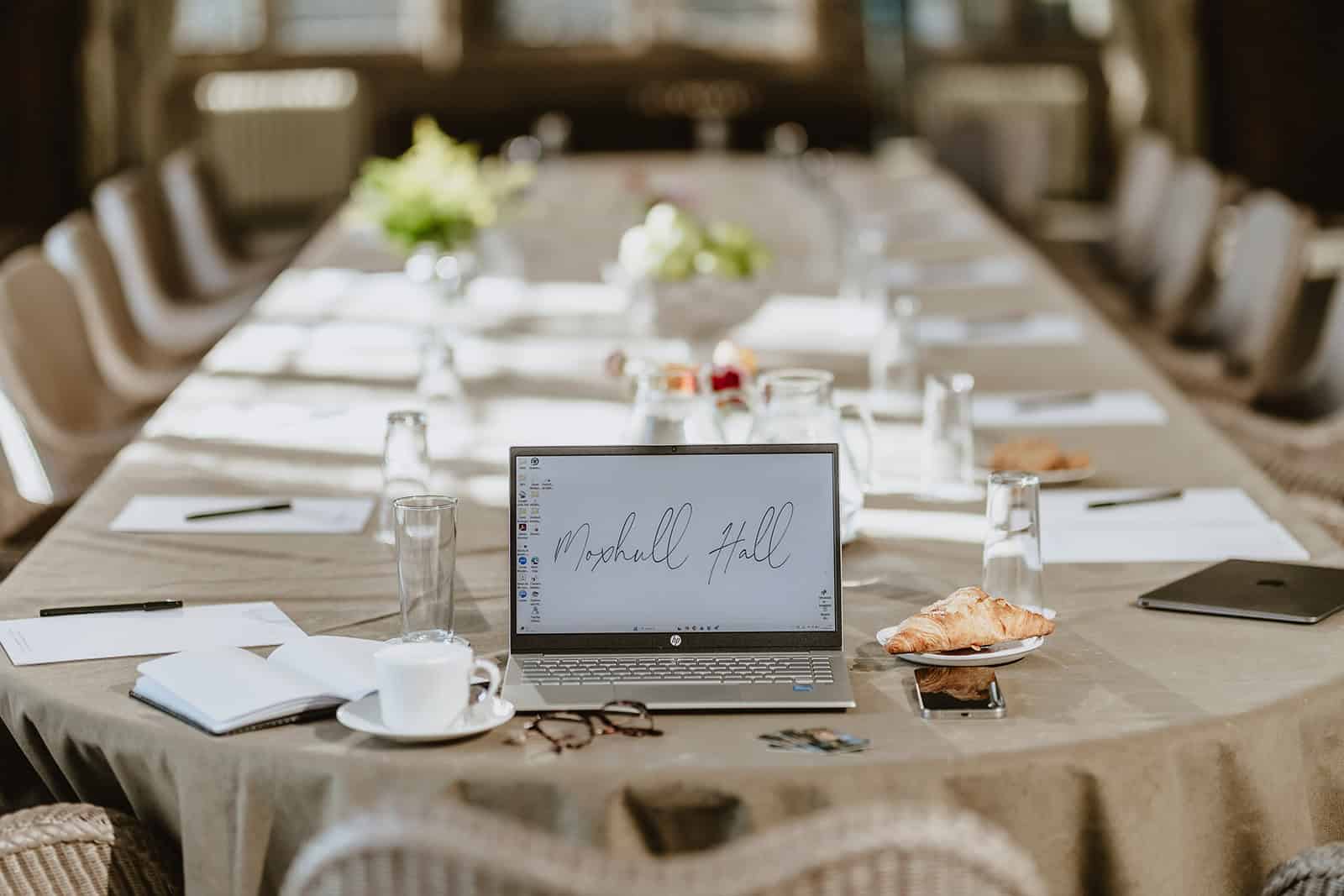 Conference room setup with laptop, glasses, and notepads on a long table.