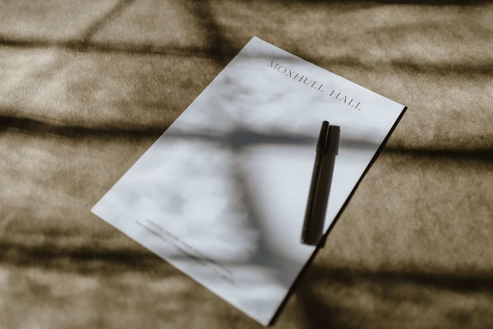 Moleskine notebook with a pen on a textured surface, shadowed by leaves.
