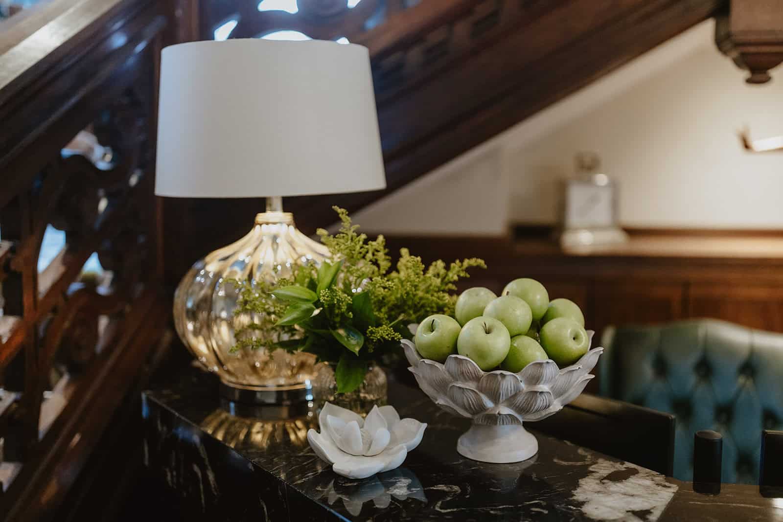 Elegant interior with a lamp, bowl of green apples, and floral decor in a cosy setting.