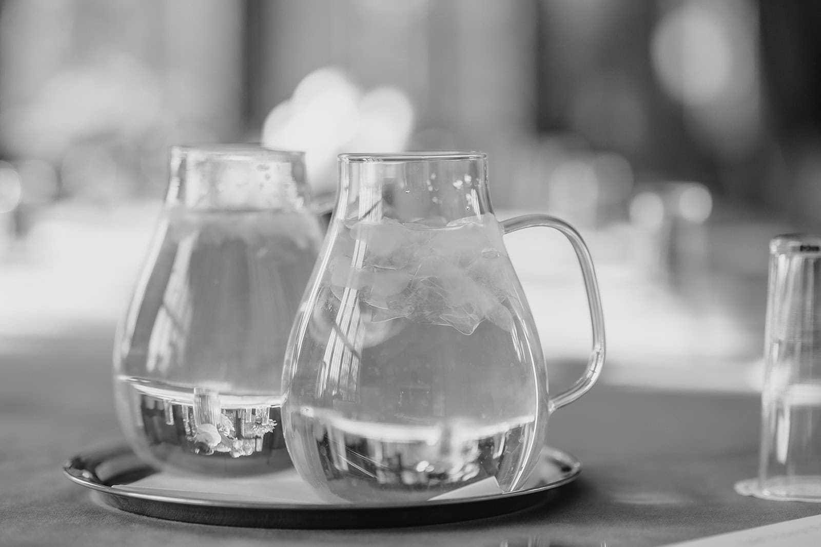 Two glass pitchers of water on a tray in black and white.