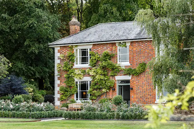 Traditional brick house with ivy and lush garden in a peaceful setting.