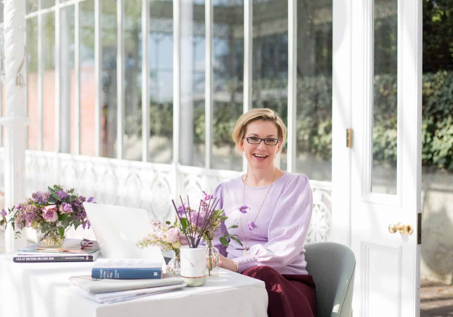 Lady wearing lavender sitting at a table working on an apple mac