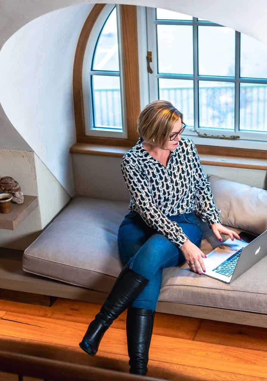 Woman working on a laptop in a cosy attic space with large window.