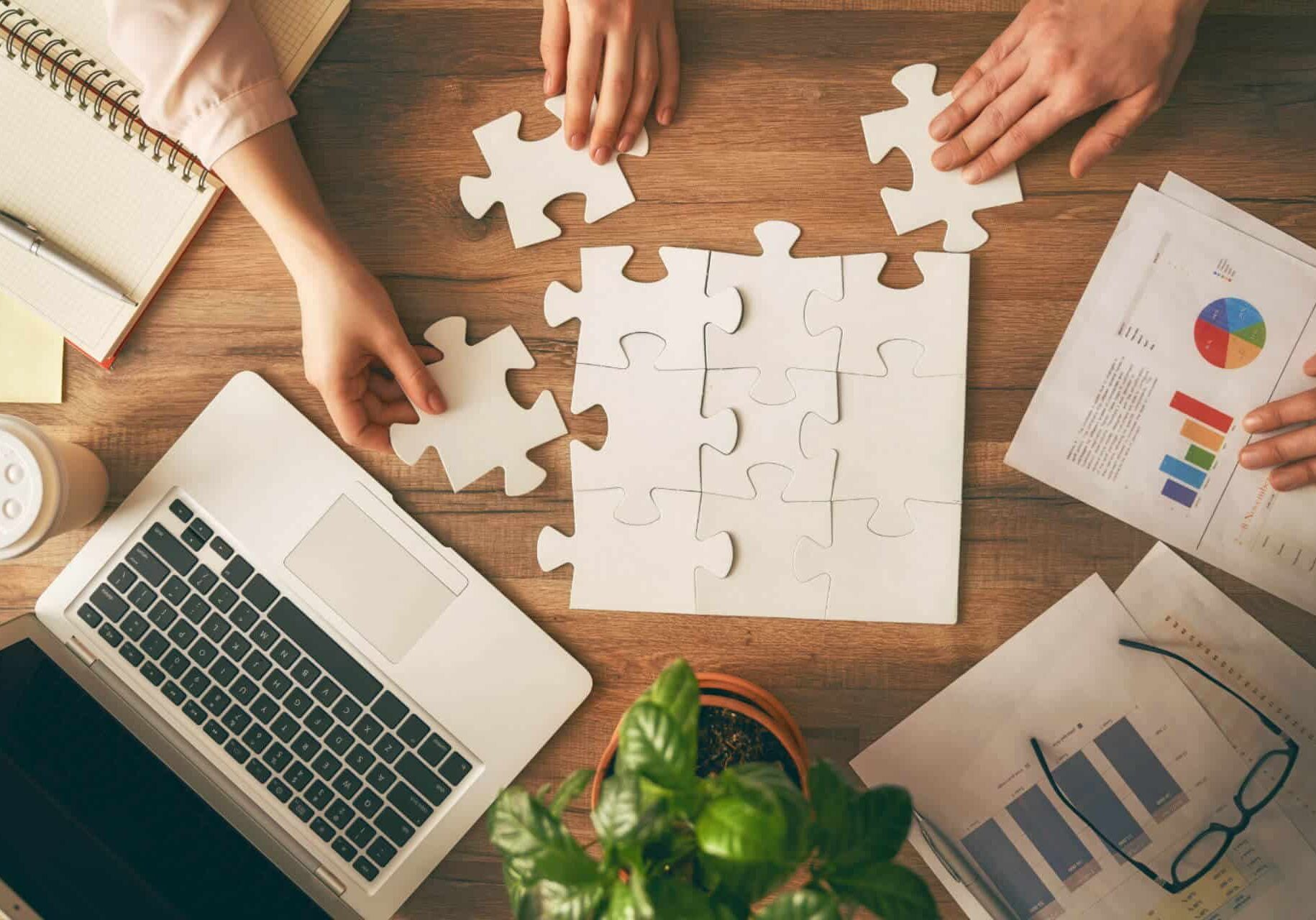 Lap-top-and-scattered-notes-showing-graphs-and-pie-charts-alongside-hands-piecing-together-a-puzzle