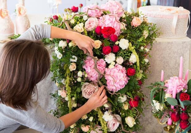 Florist at work. Woman making spring floral decorations the wedding table the bride and groom. Flowers candles a bottle of champagne. The vintage.